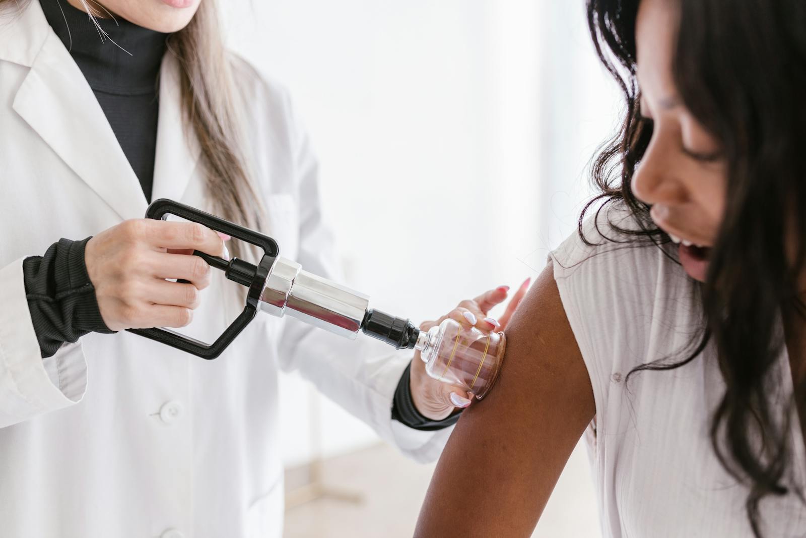 Asian acupuncturist performs cupping therapy on a woman's arm in a bright therapy room.